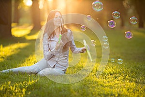 Young spring fashion casual woman blow bubbles in the sunset in