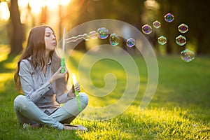 Young spring fashion casual woman blow bubbles in the sunset in