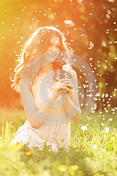 Young spring fashion woman blowing dandelion in spring garden. S