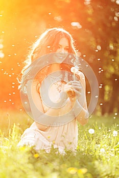 Young spring fashion woman blowing dandelion in spring garden. S