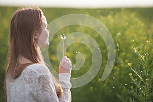 Young spring fashion woman blowing dandelion in spring garden. Springtime. Trendy girl at sunset in spring landscape background.