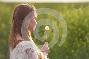 Young spring fashion woman blowing dandelion in spring garden. Springtime. Trendy girl at sunset in spring landscape background.