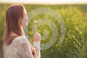 Young spring fashion woman blowing dandelion in spring garden. Springtime. Trendy girl at sunset in spring landscape background.