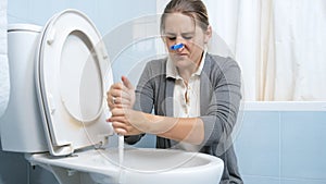 Young squeamish woman with clothesping on her nose washing dirty toilet