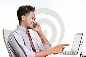 Young business man smiling while talking on the phone and working with laptop computer