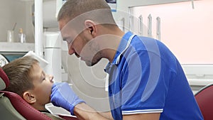 Young stomatologist in rubber gloves puts orthodontics plate on teeth to child in hospital next to modern equipment