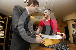 Young store clear cutting cheese for businessman