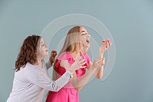 Young stout woman trying to stop her slim friend from eating donut on color background. Diet food concept