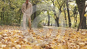 Young streetstyle casual man in sunglasses walking in the autumn park and kick the piles of yellow maple leaves