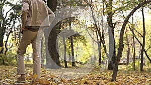 Young streetstyle casual man in sunglasses walking in the autumn park and kick the piles of yellow maple leaves