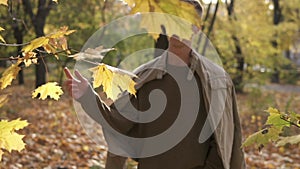 Young streetstyle casual man in sunglasses walking in the autumn park and tore off the yellow maple leaf