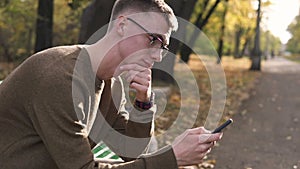 Young streetstyle man on the banch enjoy using his smartphone in park, Young caucasian man in glasses
