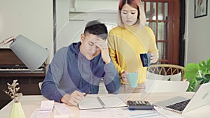 Young stressed asian couple managing finances, reviewing their bank accounts using laptop computer and calculator at modern home.