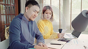 Young stressed asian couple managing finances, reviewing their bank accounts using laptop computer and calculator at modern home.