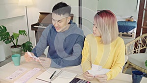 Young stressed asian couple managing finances, reviewing their bank accounts using laptop computer and calculator at modern home.