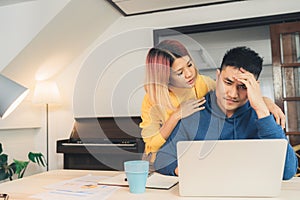 Young stressed asian couple managing finances, reviewing their bank accounts using laptop computer and calculator at modern home.