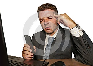 Young stressed businessman in suit and tie working overwhelmed at office laptop computer desk suffering headache cause of work