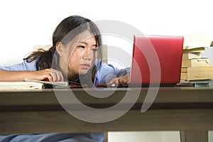Young stressed and frustrated Asian Korean student girl working hard with laptop computer and books pile on desk overwhelmed and photo