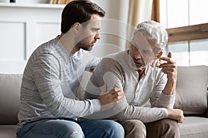 Young stressed man comforting irritated mature old father.