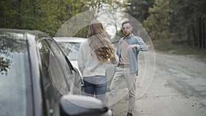 Young stressed man and woman yelling and gesturing on roadside. Angry Caucasian millennial drivers in car accident