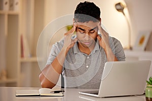 Young stressed man working alone on a laptop in an office at night. Guy looking tired and worried while struggling with