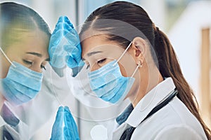 Young stressed and overworked doctor wearing mask and gloves while standing at a window in a hospital or clinic. One