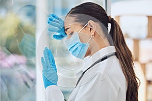 Young stressed and overworked doctor wearing mask and gloves while standing at a window in a hospital or clinic. One