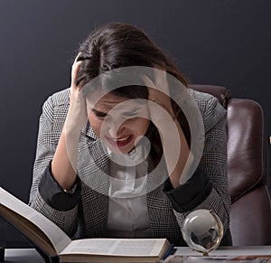 Young stressed student girl studying pile of books on library desk preparing test or exam in stress feeling