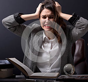 Young stressed student girl studying pile of books on library desk preparing test or exam in stress feeling