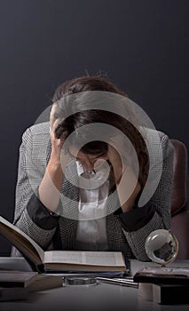 Young stressed student girl studying pile of books on library desk preparing test or exam in stress feeling