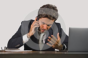 young stressed and upset business man working at office computer desk talking frustrated on mobile phone feeling tired