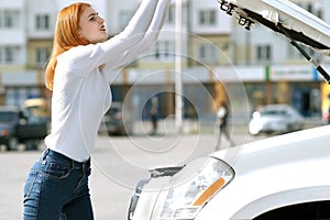 Young stressed woman driver near broken car with popped hood having a prbreakdown problem with her vehicle waiting for assistance