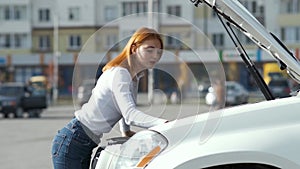 Young stressed woman driver near broken car with popped hood having a prbreakdown problem with her vehicle waiting for assistance.