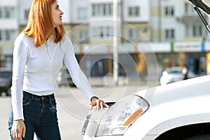 Young stressed woman driver near broken car with popped hood having a prbreakdown problem with her vehicle waiting for assistance