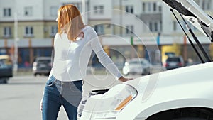 Young stressed woman driver near broken car with popped hood having a prbreakdown problem with her vehicle waiting for assistance.