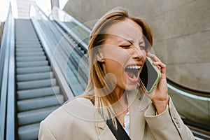 Young stressed woman screaming into the phone with closed eyes