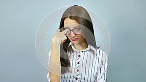 Young strict exacting female teacher wearing optical eyeglasses looking at the camera in studio on grey background