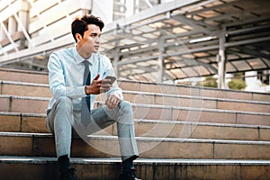 Young Striving Asian Businessman Sitting on Staircase in the City. Using Mobile Phone photo