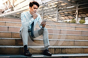Young Striving Asian Businessman Using Mobile Phone in the City. Sitting on Staircase. Reading Seriously topic photo