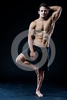 Young strong athlete is making yoga on black background