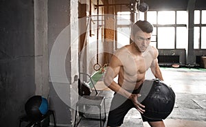 Young strong fit muscular man doing throwing medicine ball up on the wall for crossfit training hard core workout in gym