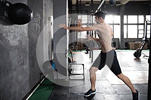 Young strong fit muscular man doing throwing medicine ball up on the wall for crossfit training hard core workout in gym