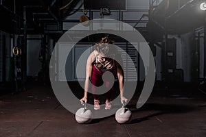 Young strong fit sweaty muscular girl with big muscles doing push ups on two big old heavy kettlebells with her hands for hard cor