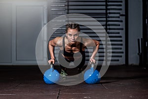 Young strong fit sweaty muscular girl with big muscles doing push ups on two big old heavy kettlebells with her hands for hard cor