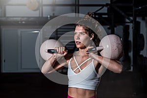 Young strong fit sweaty muscular girl with big muscles holding two big old kettlebells with her hands on her shoulders for hard co