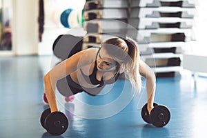 Young strong girl doing push-ups on dumbbells in the gym