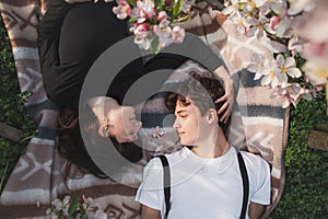 Young strong love between two young people lying on a blanket under apple trees. Candid portrait of a couple in casual clothes