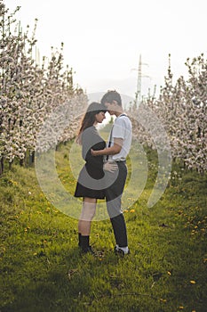 Young strong love between two young people standing under apple trees. Candid portrait of a couple in casual clothes. Affection of