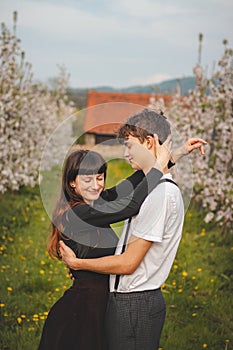 Young strong love between two young people walking under apple trees. Candid portrait of a couple in casual clothes. Affection of