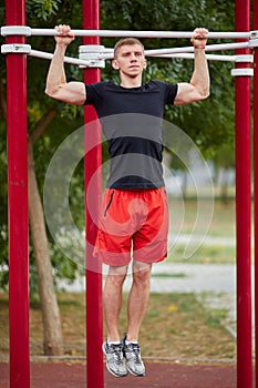 Young strong man does pull-ups on a horizontal bar on a sports ground in the summer in the city.